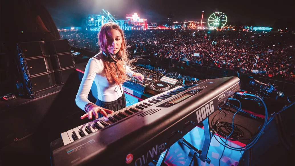 Photo of LP Giobbi behind a piano on stage at a huge colourful music festival