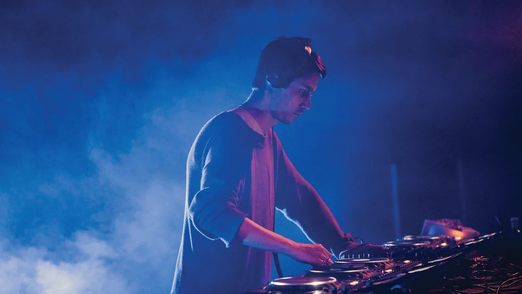 Side profile image of Call Super behind the decks on a smoky stage