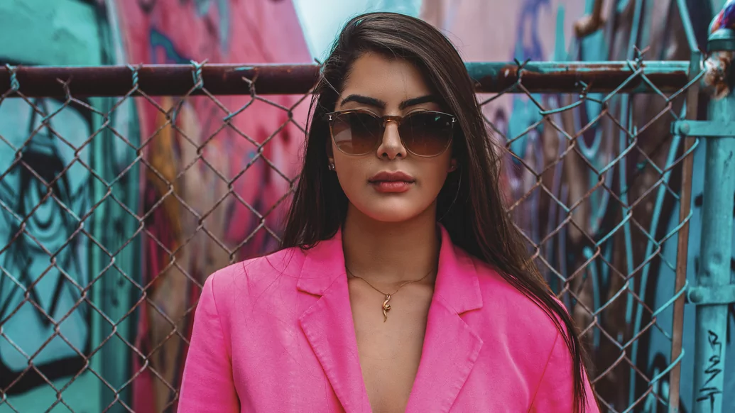 Photo of Amal Nemer wearing a pink suit and big sunglasses in front of a graffitied alleyway