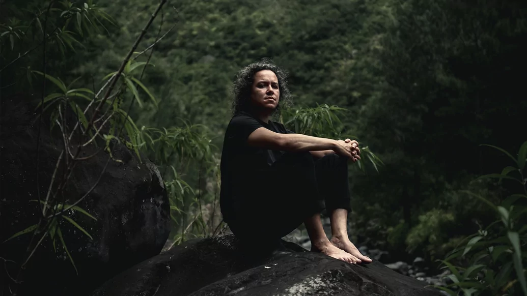 Photo of Labelle sitting on a rock in the jungle wearing a black outfit