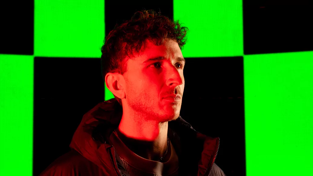 Photo of RL Grime wearing a black puffer jacket in front of a green and black background