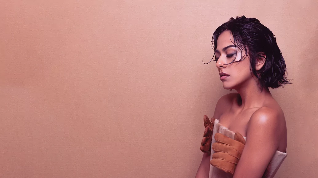 Photo of Arushi Jain wearing a beige dress with glove details against a brown background