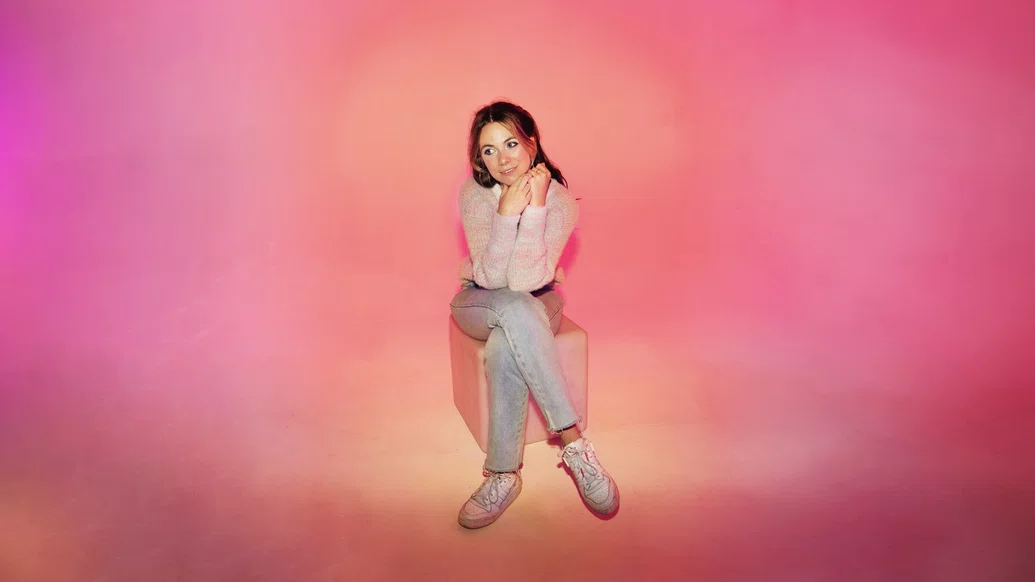 Photo of Bad Snacks wearing a pink and blue jumper against a pink background