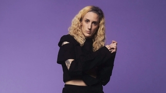 Photo of Lauren Flax wearing a ripped black jumper in front of a purple background