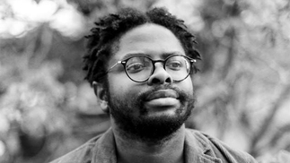Black and white photo of a man with short dreadlocks and glasses