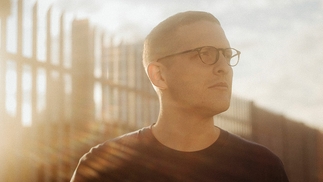 Floating Points poses by a fence in low sunlight