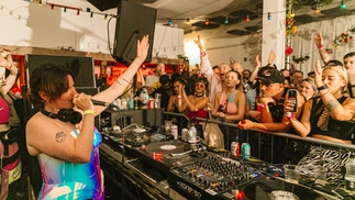 Photo of Saoirse DJing at Body Movements festival. She is talking into a mic with one arm held high