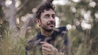 Photo of Dualist Inquiry crouching in grass while wearing a navy sweater