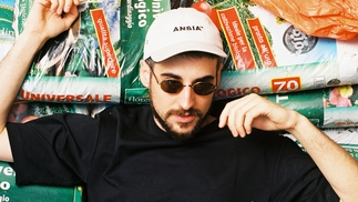 Photo of Piezo lying on a pile of bags of soil wearing a black t-shirt, white hate and sunglasses