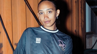 Photo of Aletha in a metallic blue-grey Jersey standing next to a wooden wall