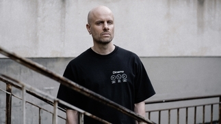 Photo of Kuttin Edge wearing a black t-shirt and standing on a grey industrial staircase