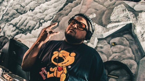 Photo of DJ Deeon DJing in sunglasses, wearing a t-shirt with a bear on it