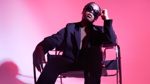 Photo of Karen Nyame KG. She's sitting with a powerful stance in a metal armchair, wearing a dark suit and shades