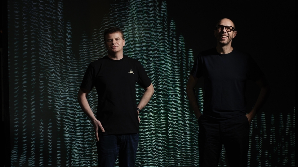 Photo of Tom Rowlands and Ed Simons from The Chemical Brothers smiling in front of a black and green electronic screen