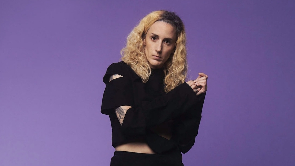 Photo of Lauren Flax wearing a ripped black jumper in front of a purple background